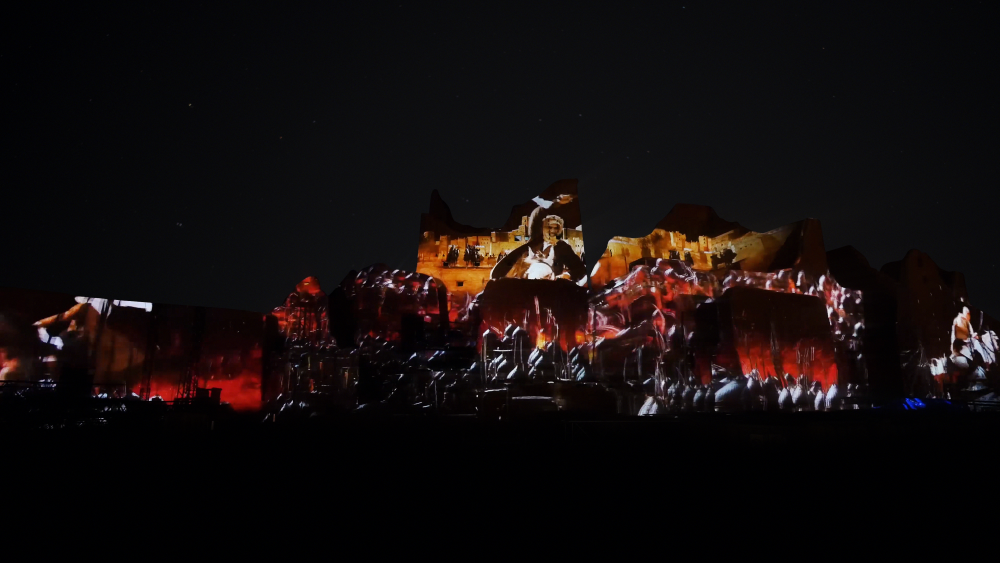 Large stage concert with dramatic red and orange lighting illuminating performers and crowd at night