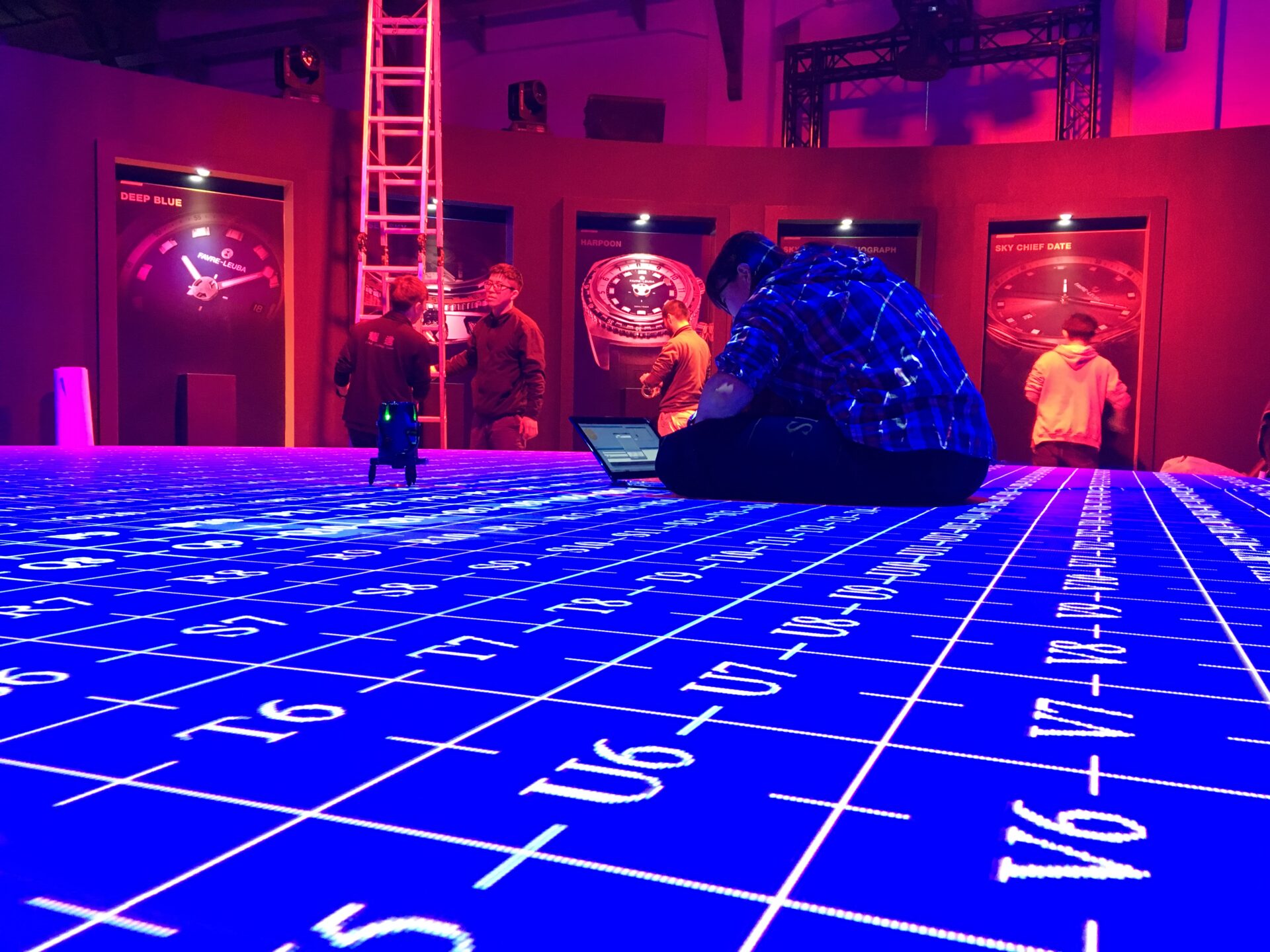 Futuristic neon-lit museum exhibit with interactive displays, blue floor grid, and pink-red wall lighting