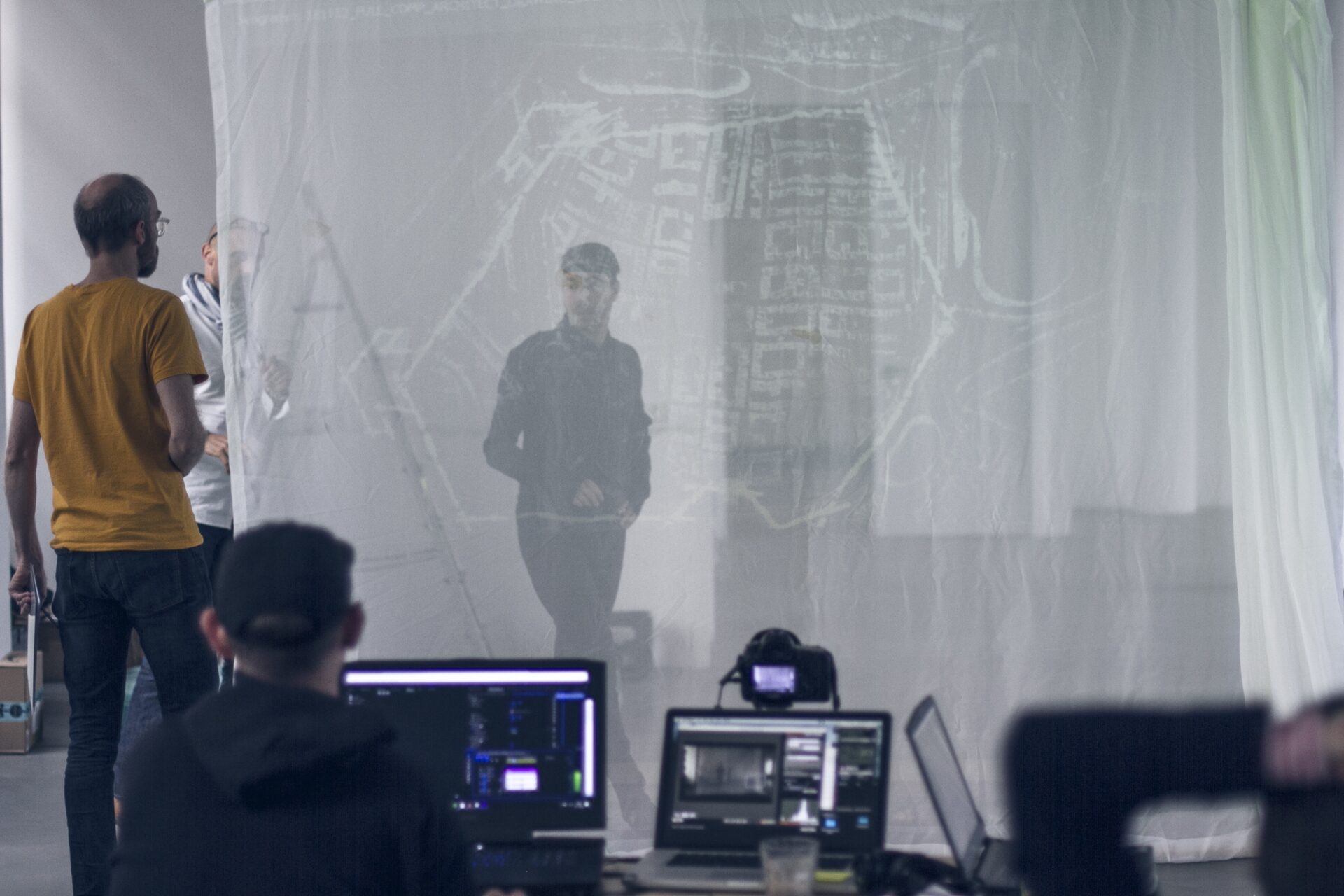 Person in yellow shirt viewing architectural blueprints projected on translucent screen during presentation