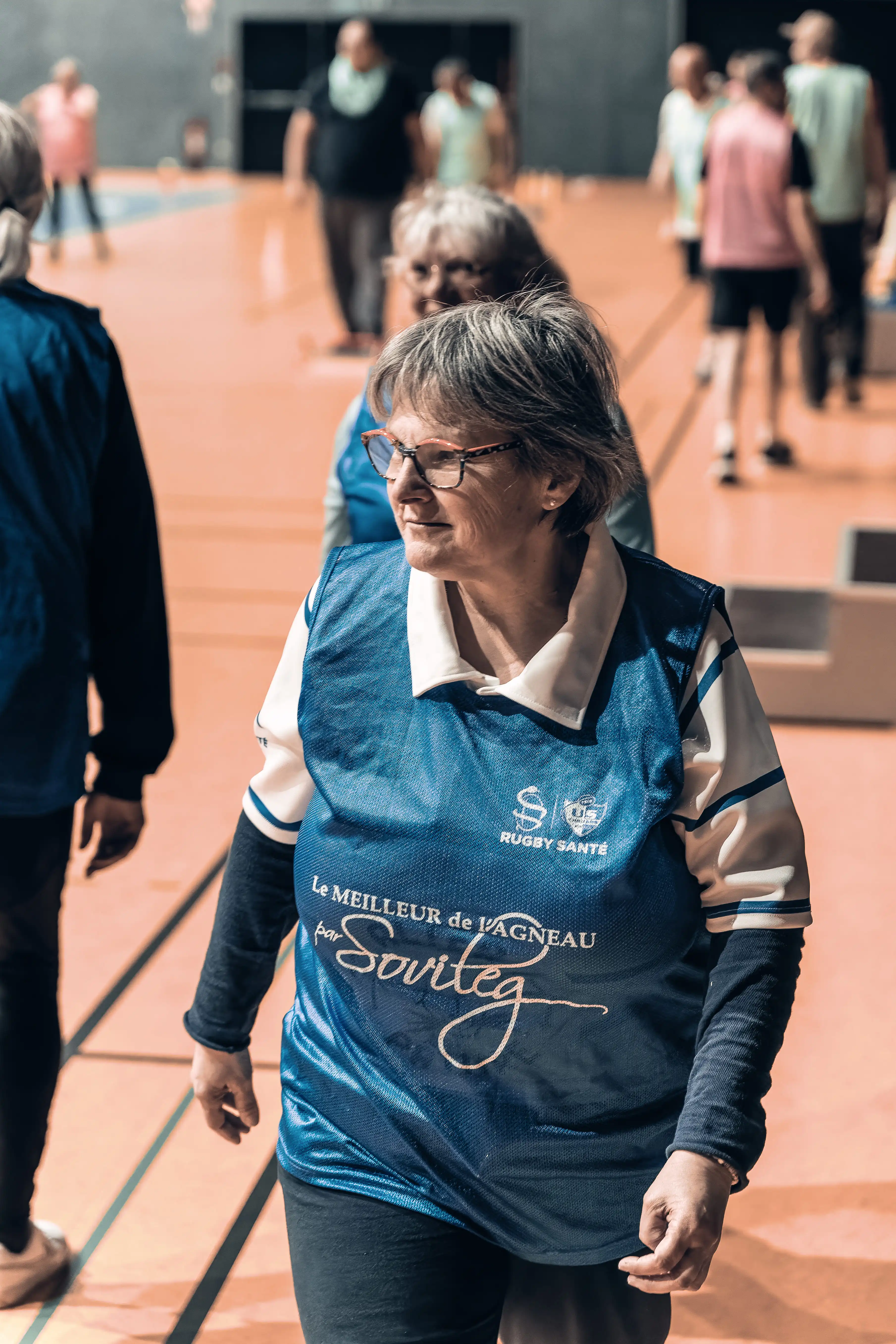 Femme âgée portant un maillot bleu avec l'inscription Rugby Santé lors d'une activité en salle de sport.