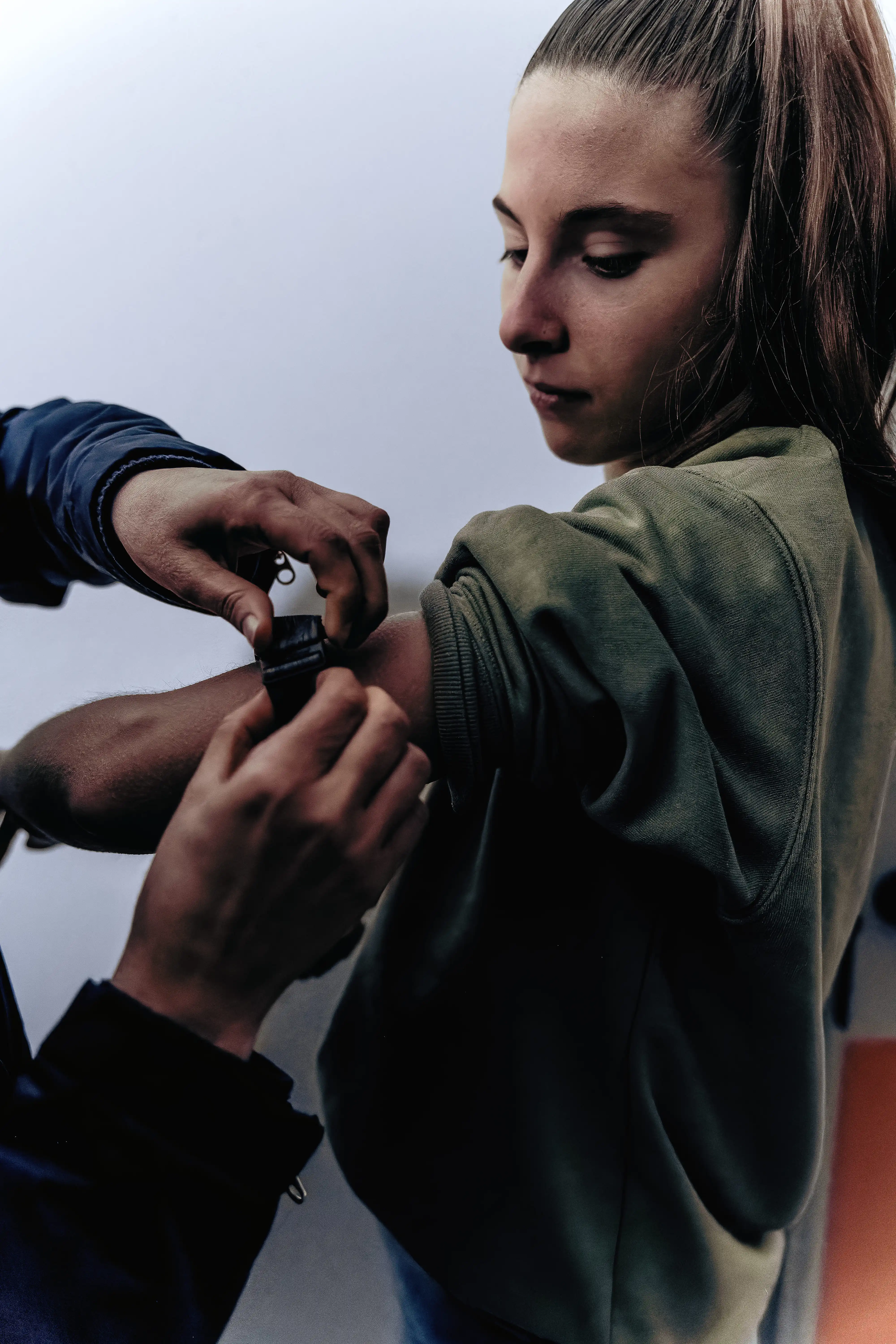 Une jeune femme regarde son bras pendant qu'une autre personne lui attache un capteur de fréquence cardiaque autour du bras.