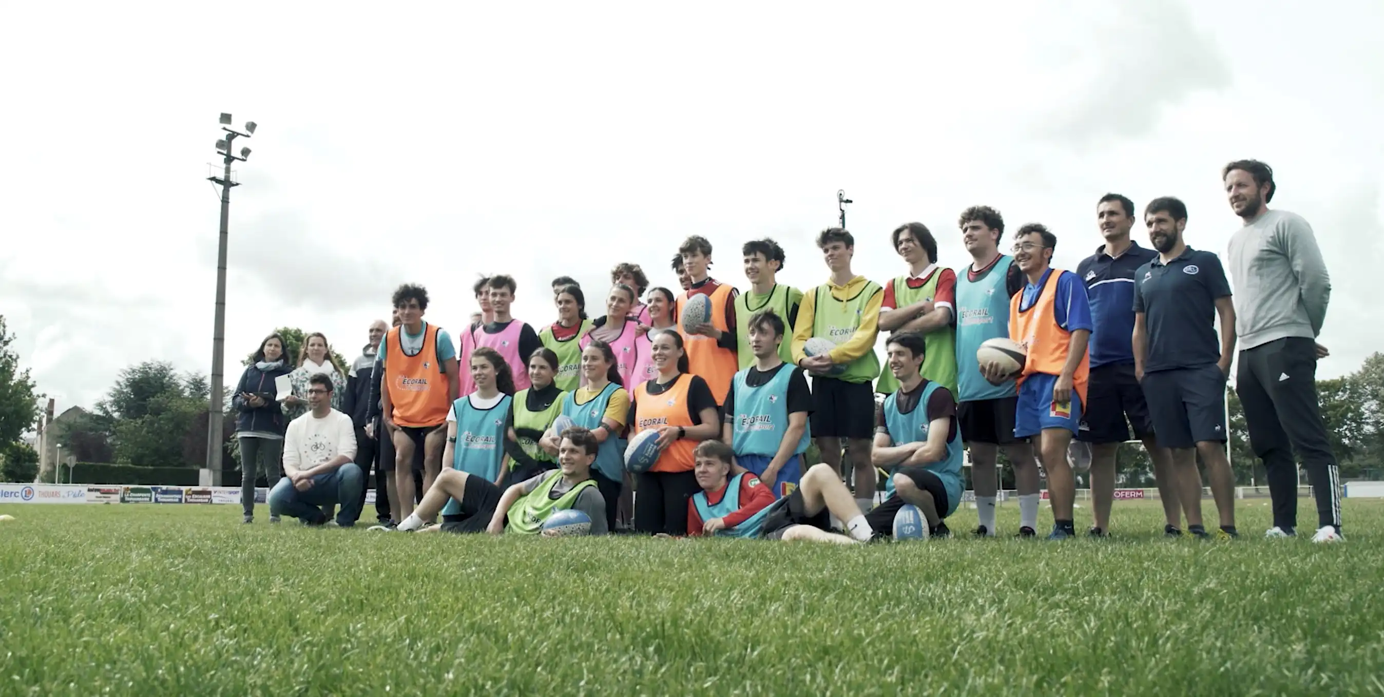 Groupe de jeunes joueurs de rugby posant ensemble sur un terrain gazonné lors d'une journée nuageuse.