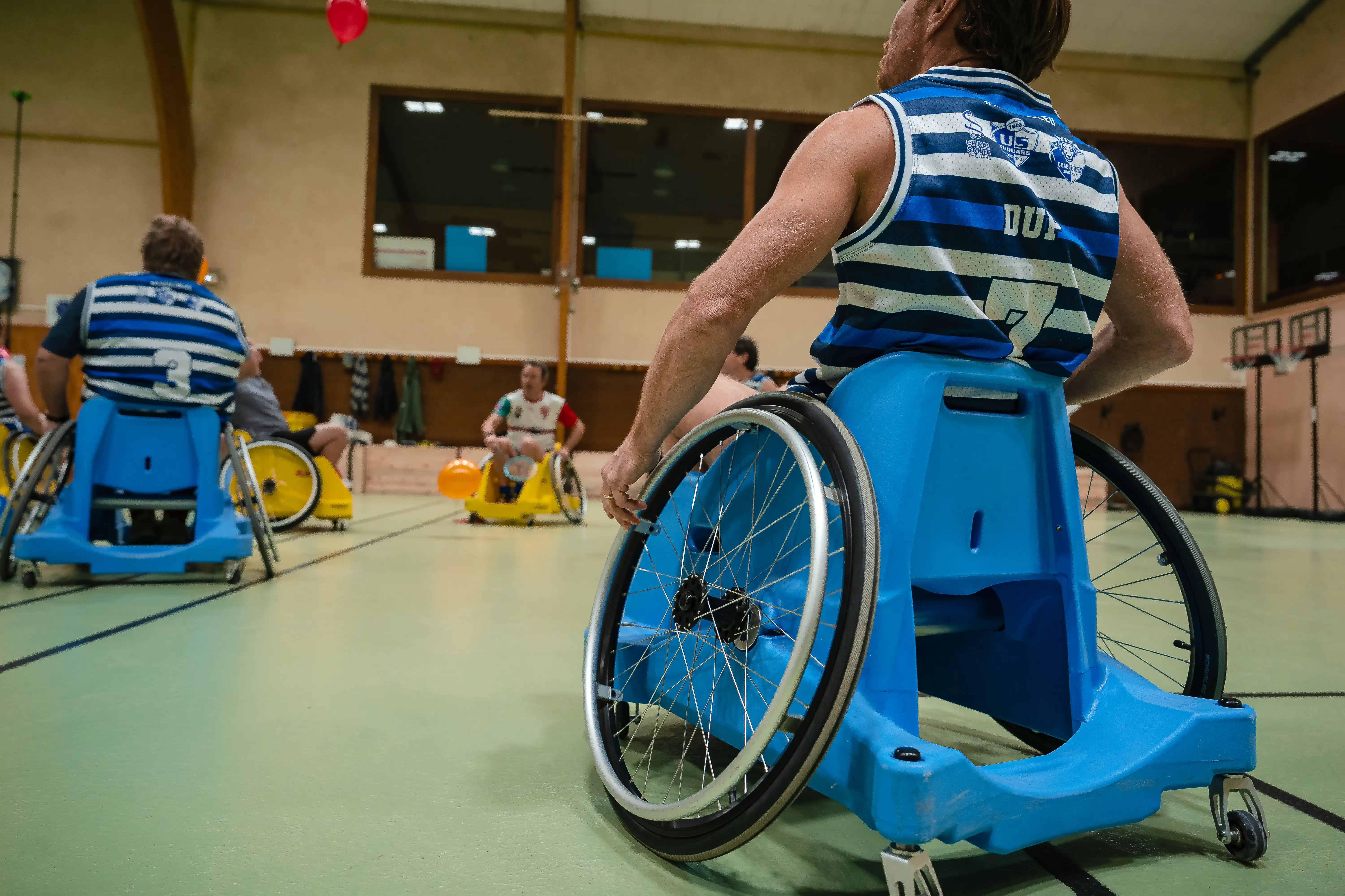 Match de rugby en fauteuil roulant avec joueurs en maillots rayés bleus et blancs dans une salle de sport.