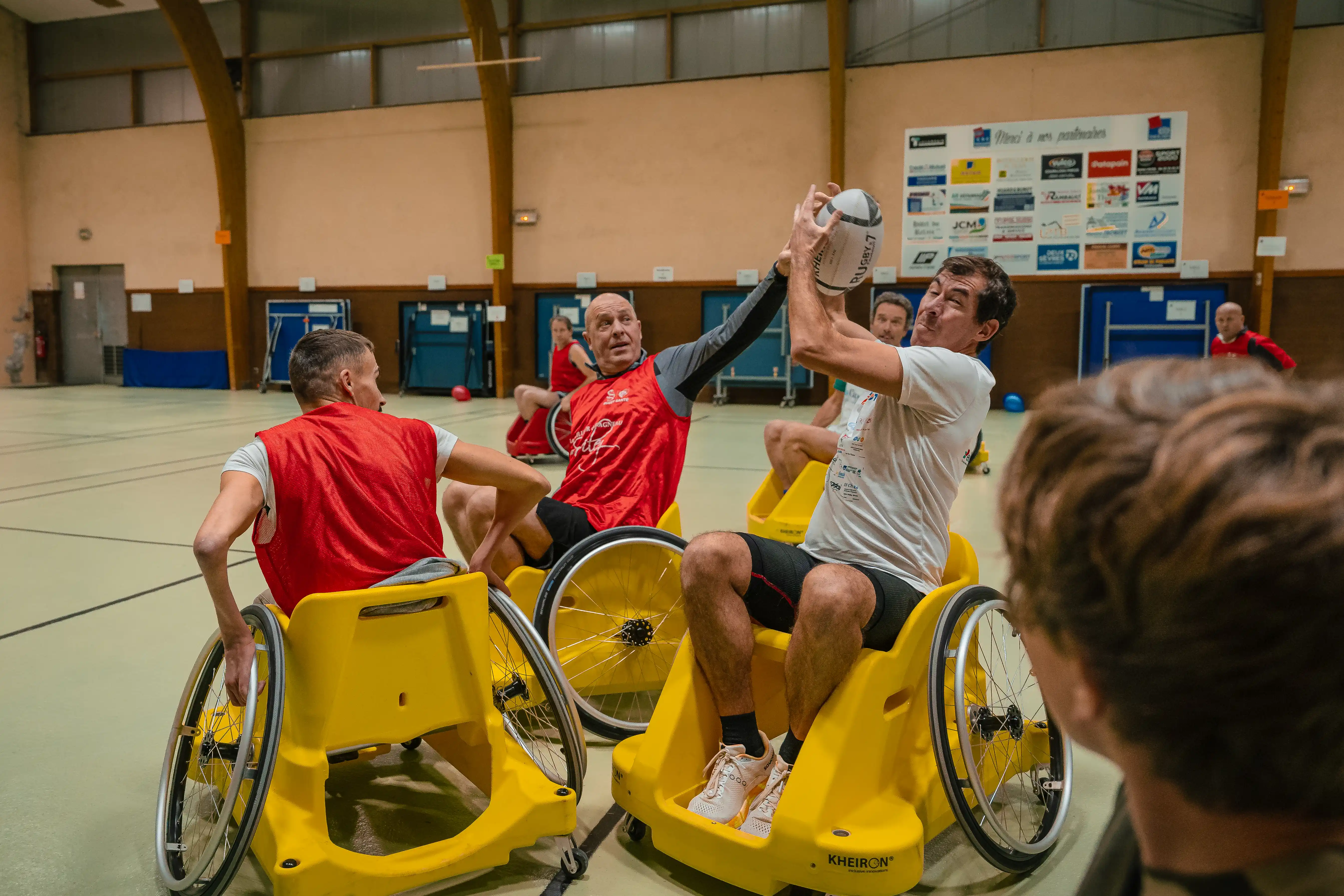 Un groupe d'hommes jouant au rugby en fauteuil roulant dans un gymnase.