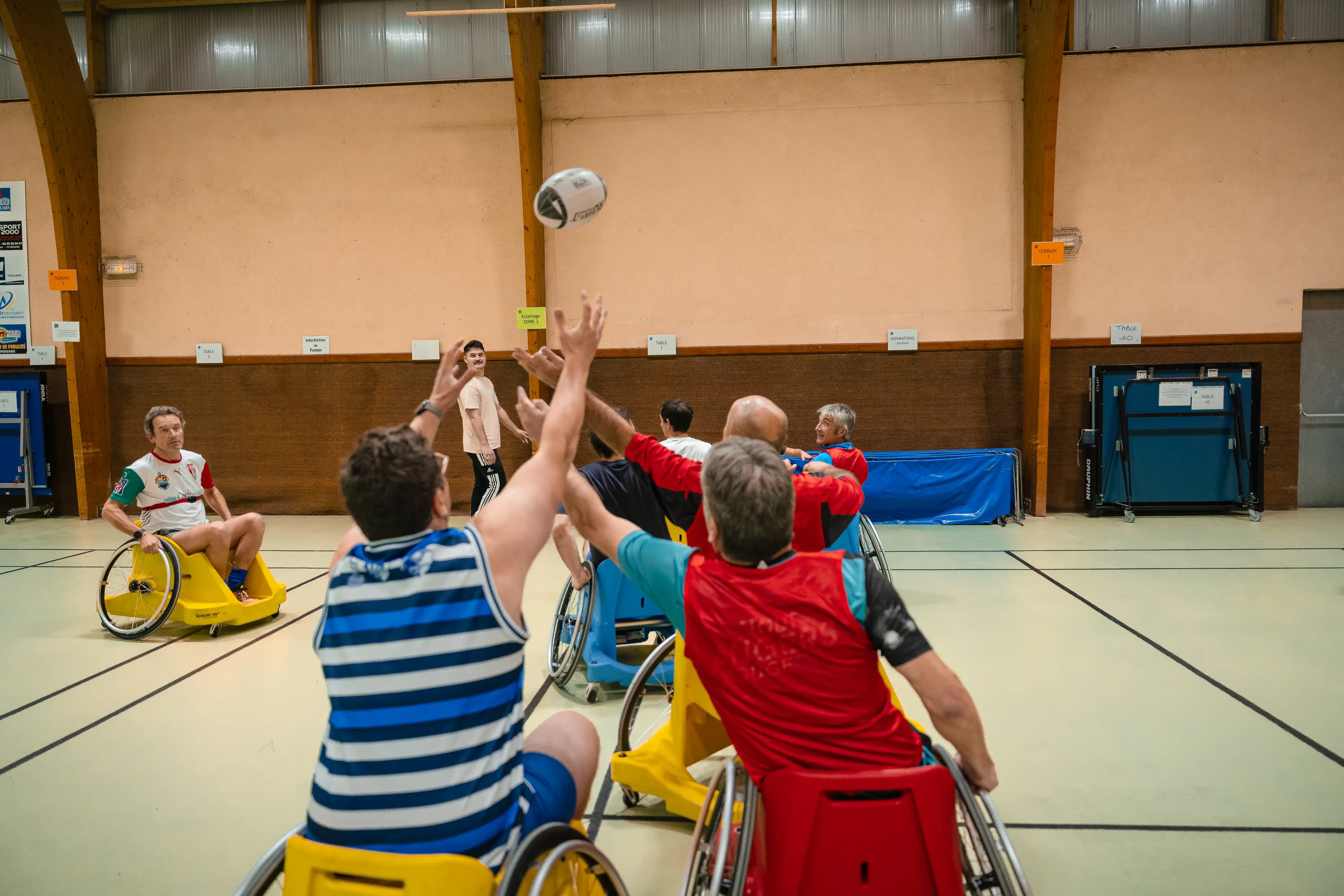 Des joueurs en fauteuil roulant jouent au rugby en salle, essayant d'attraper un ballon de rugby