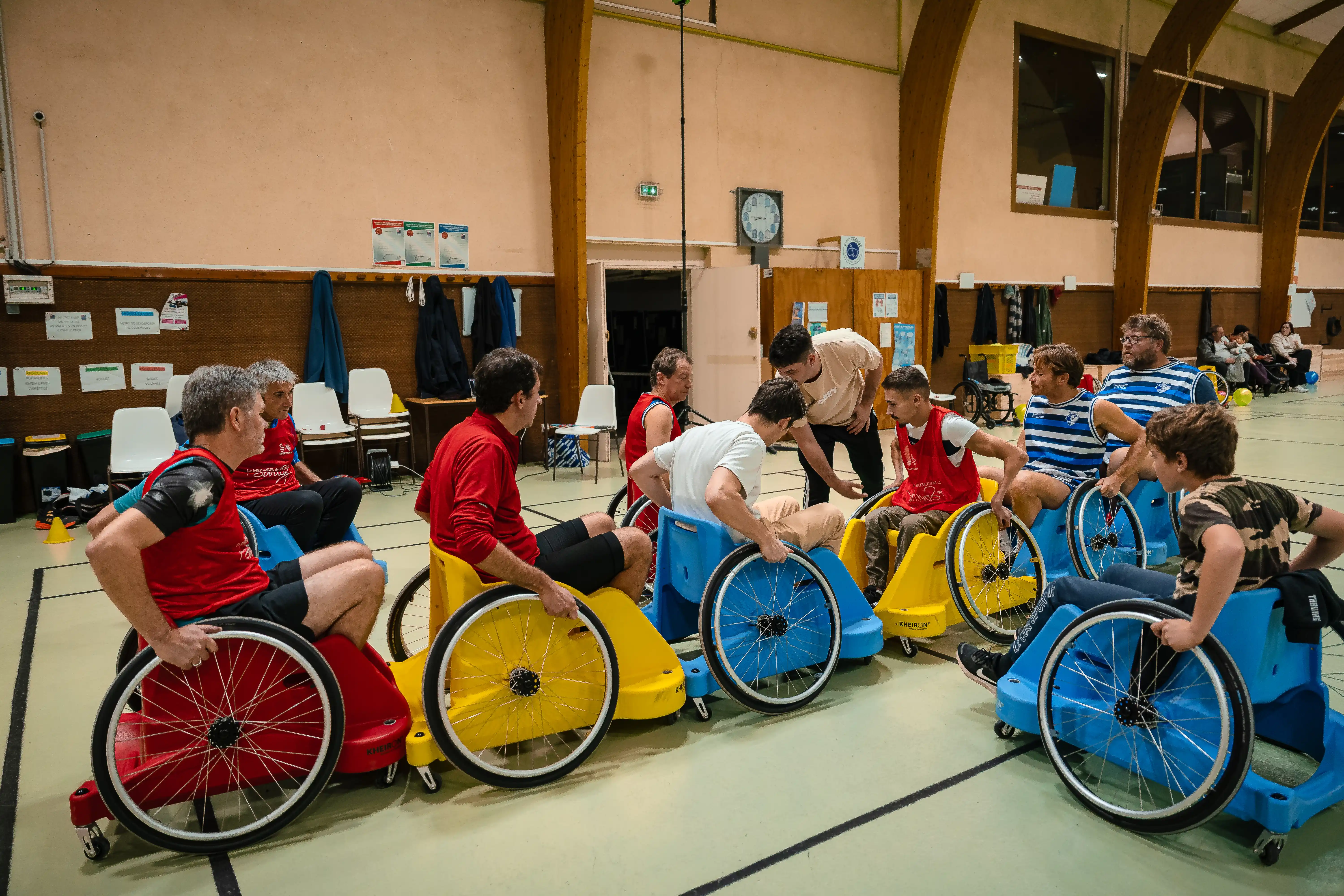 Groupe de joueurs en fauteuils roulants colorés participant à une activité sportive en intérieur.