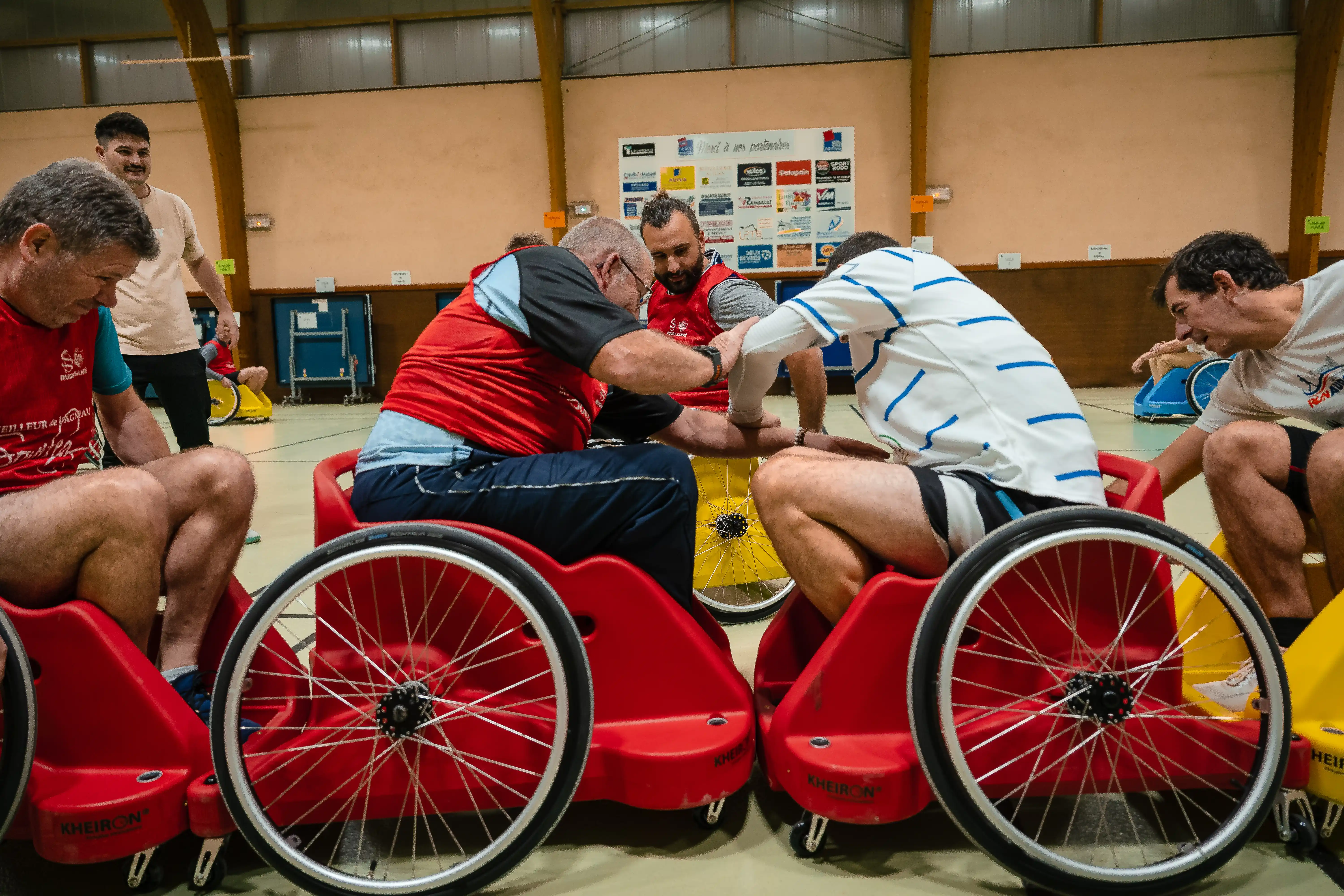 Quatre hommes en fauteuils roulants sportifs rouges jouent intensément dans un gymnase.