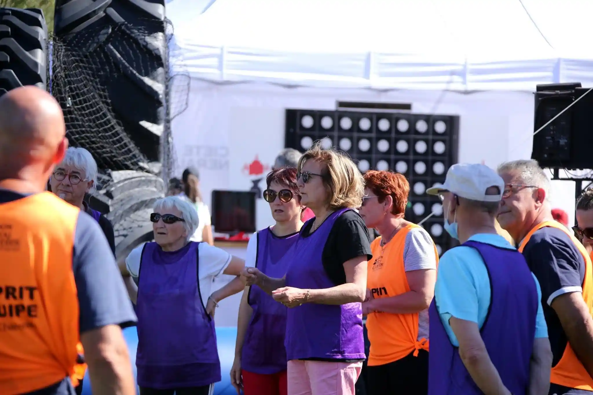 Un groupe d’adultes portant des chasubles violettes et orange discutant lors d’un événement en plein air sous un ciel clair.
