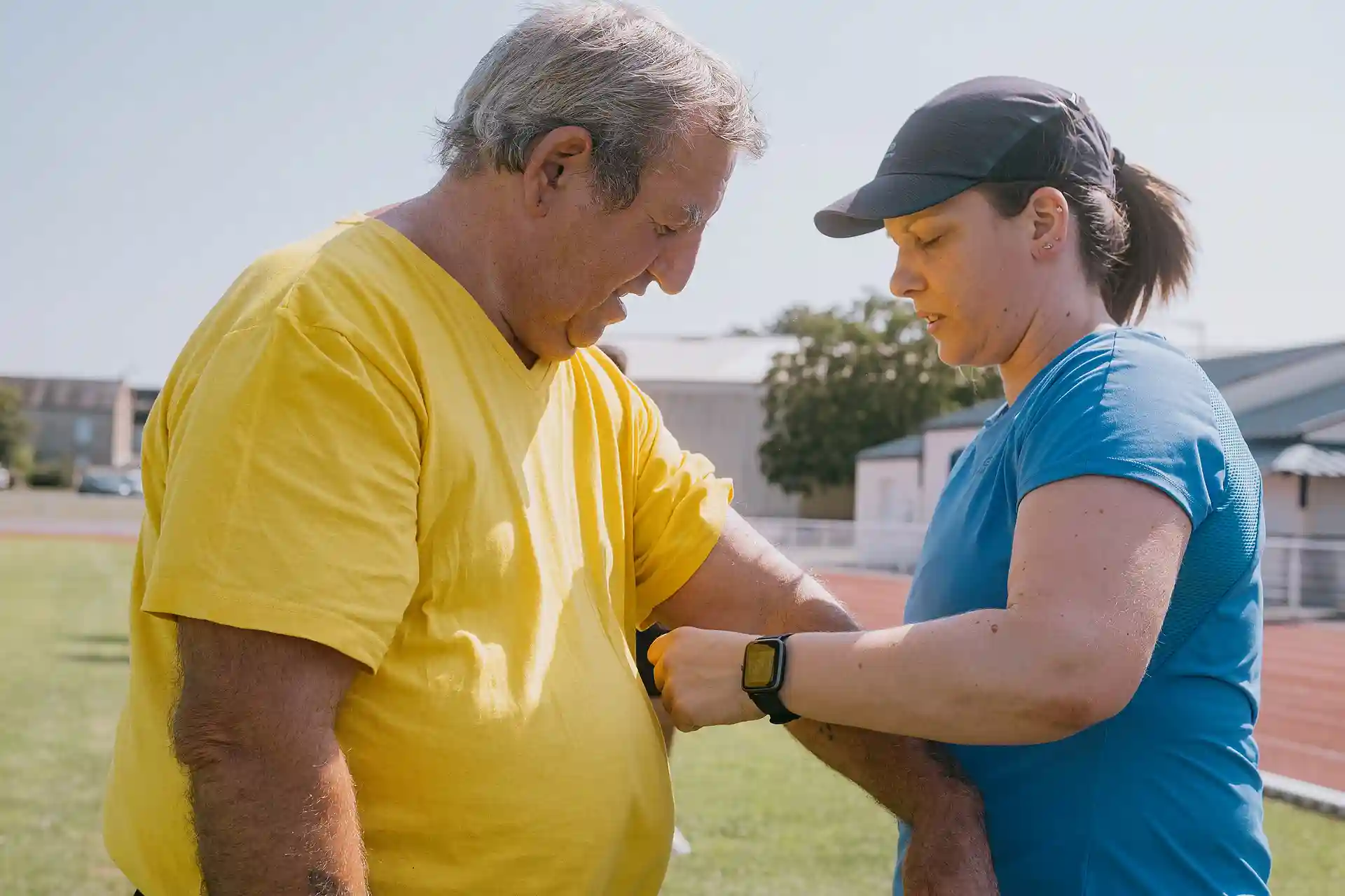 Une femme en tenue de sport aide un homme en t-shirt jaune à mettre un capteur de fréquence cardiaque autour du bras