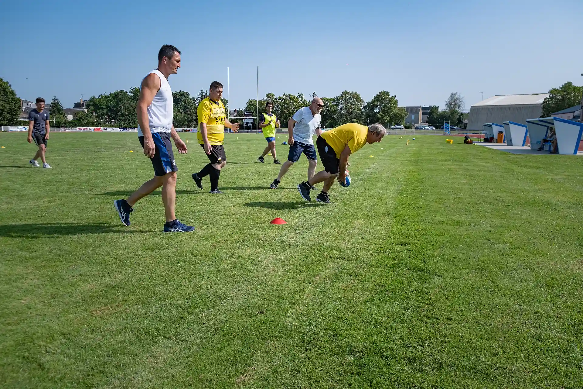 Des hommes jouant au rugby sur un terrain herbeux sous un ciel bleu clair.