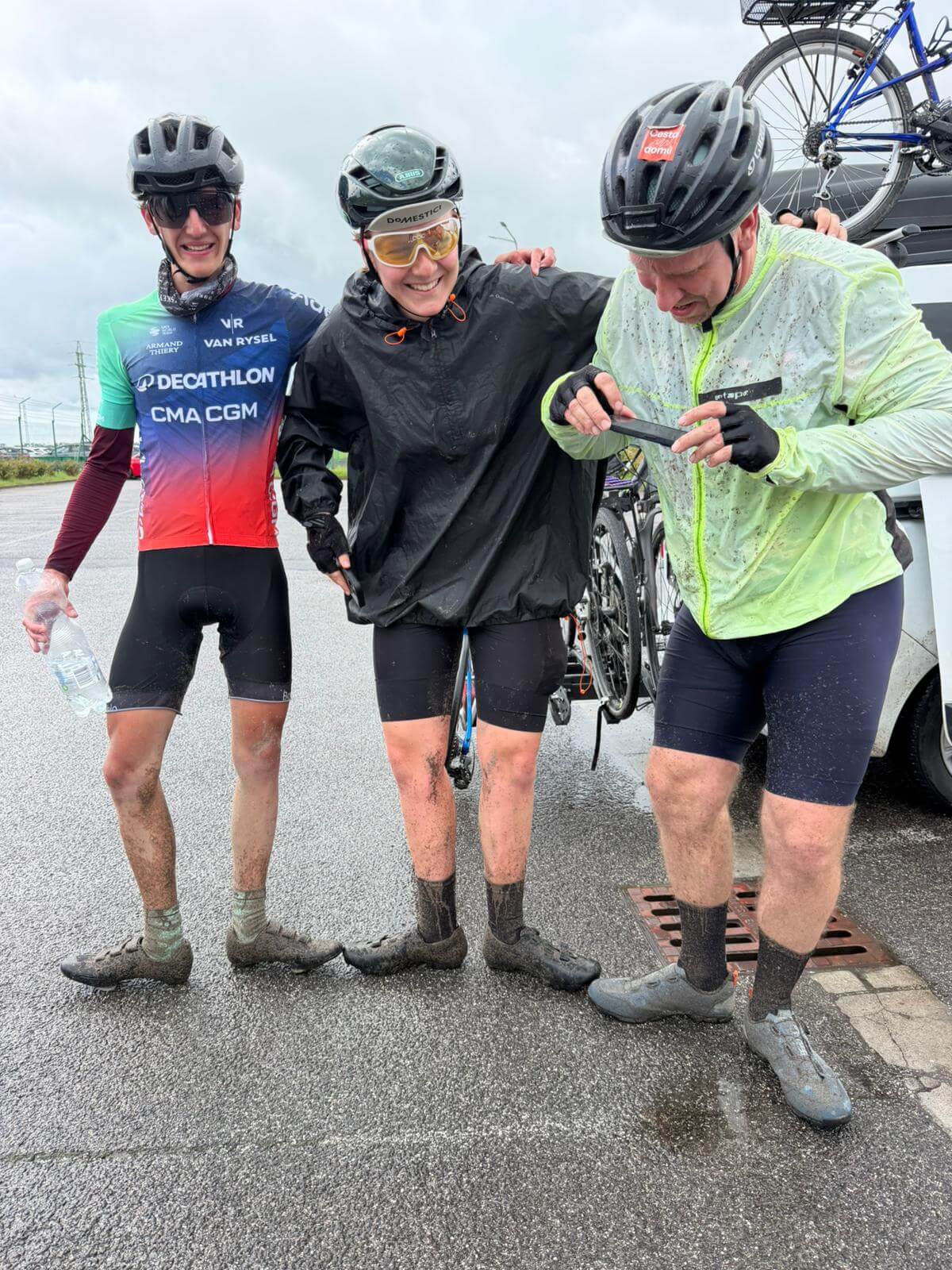 Tři blátem zbrojení cyklisté po části sobotní etapy ze Stěžer do Mělníka v rámci výzvy 8 dní pro paliativu se objímají a usmívají navzdory dešti a bahnu.