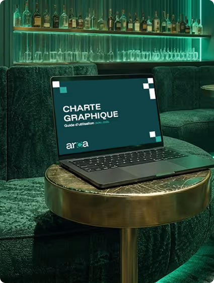 Ordinateur portable affichant une charte graphique sur une table ronde en laiton dans un salon avec un mur de bouteilles éclairé en vert.