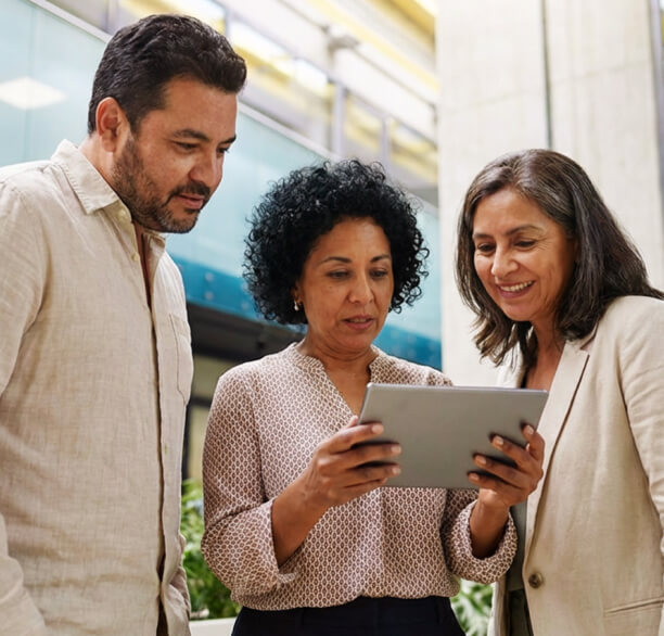 Three diverse professionals looking at a tablet together in an office space.