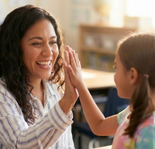 Smiling woman and young girl giving each other a high five indoors.