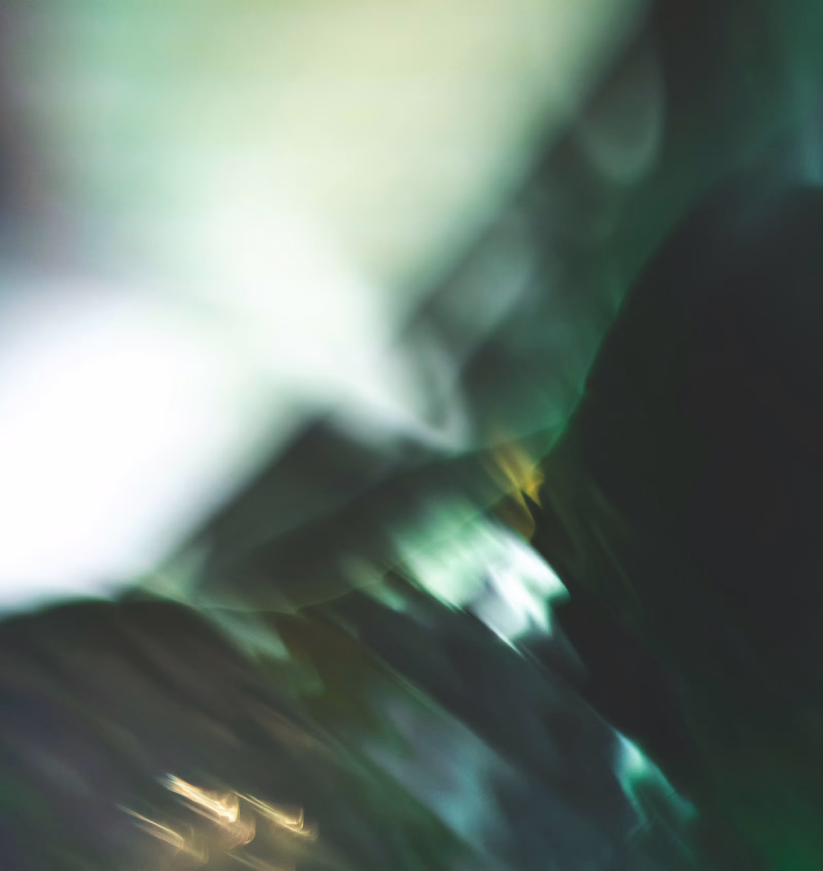 Abstract blurred image with green, white, and dark tones creating a soft, unclear pattern.