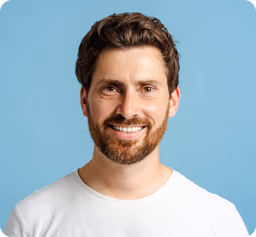 Smiling man with brown hair and beard wearing a white t-shirt against a blue background.