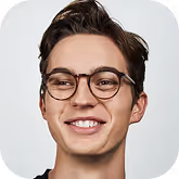 Smiling young man with short dark hair and round glasses against a plain light background.