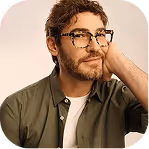 Young man with glasses resting his head on his hand, smiling thoughtfully.