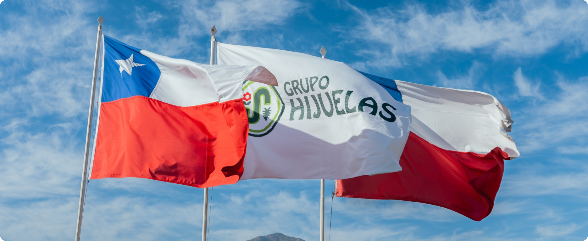 Large beige industrial fabric warehouse buildings with mountain backdrop under a partly cloudy sky.