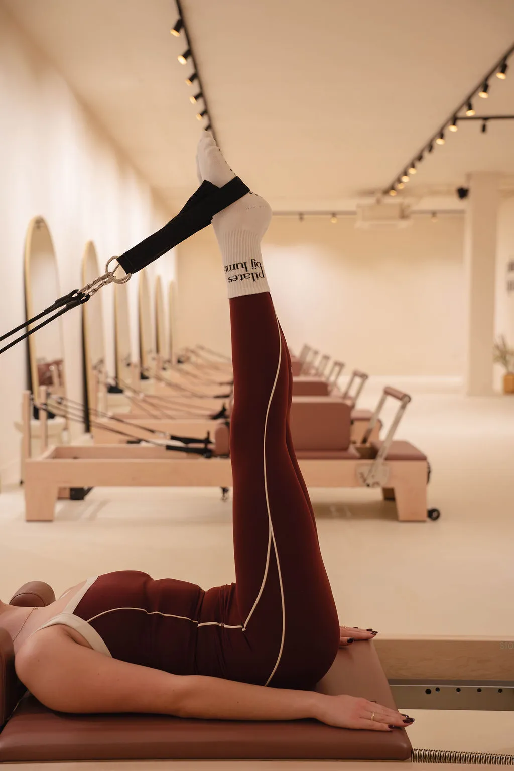 Een persoon ligt op een Pilates reformer met één been omhoog en vastgemaakt met een weerstandsband in een lichte studio.