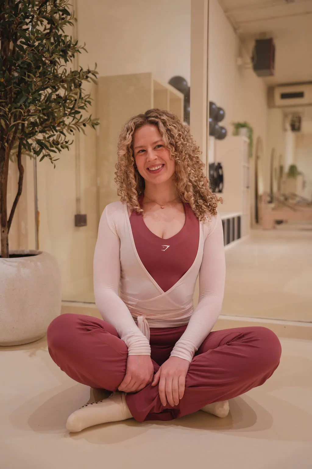 Seven women in brown workout outfits standing together smiling in a bright fitness studio.
