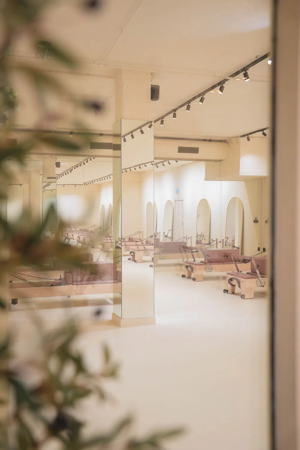 Lichte Pilatesstudio met reformerapparaten, grote spiegels en zachte verlichting.