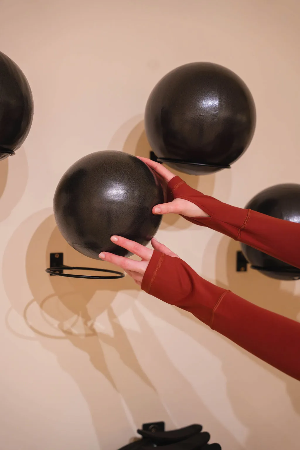 Handen, gekleed in een bordeauxrode top met lange mouwen, houden een zwarte oefenbal vast die aan de muur is bevestigd.