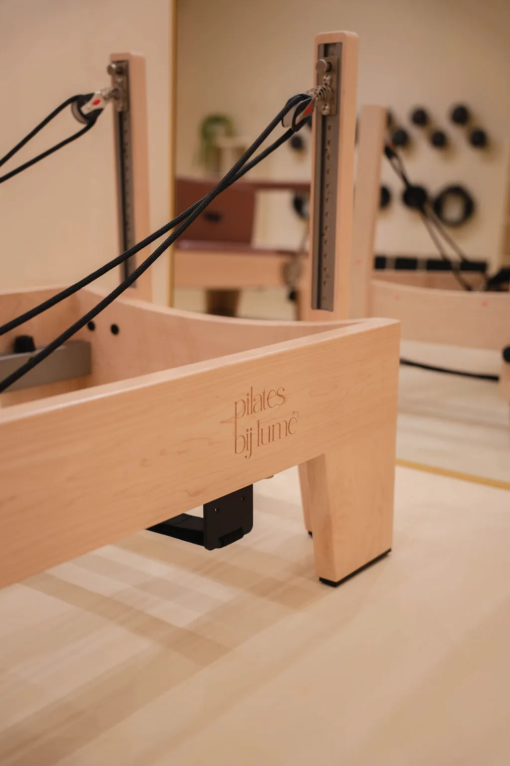 Close-up van een houten Pilates reformer met zwarte weerstandskoorden in een studio-omgeving.