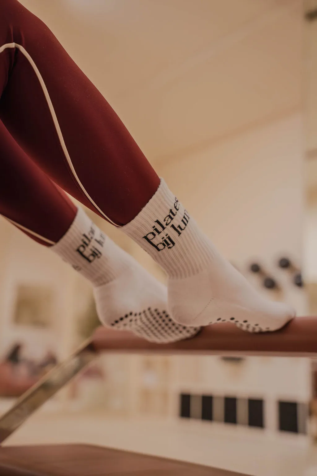 Voeten met beige antislipsokken met witte strepen op een beige footbar van een pilates reformer.