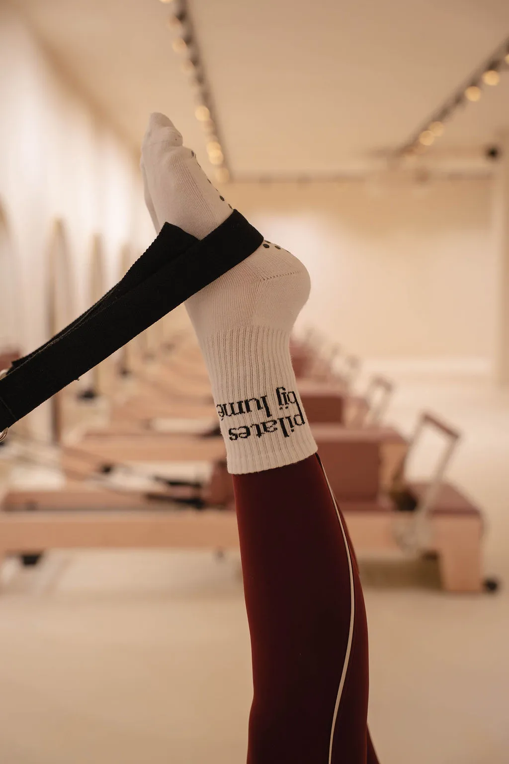 Persoon met witte legging en antislipsokken voert Reformer Pilates-oefeningen uit op een reformer met een zwarte bal achter een gebogen knie.