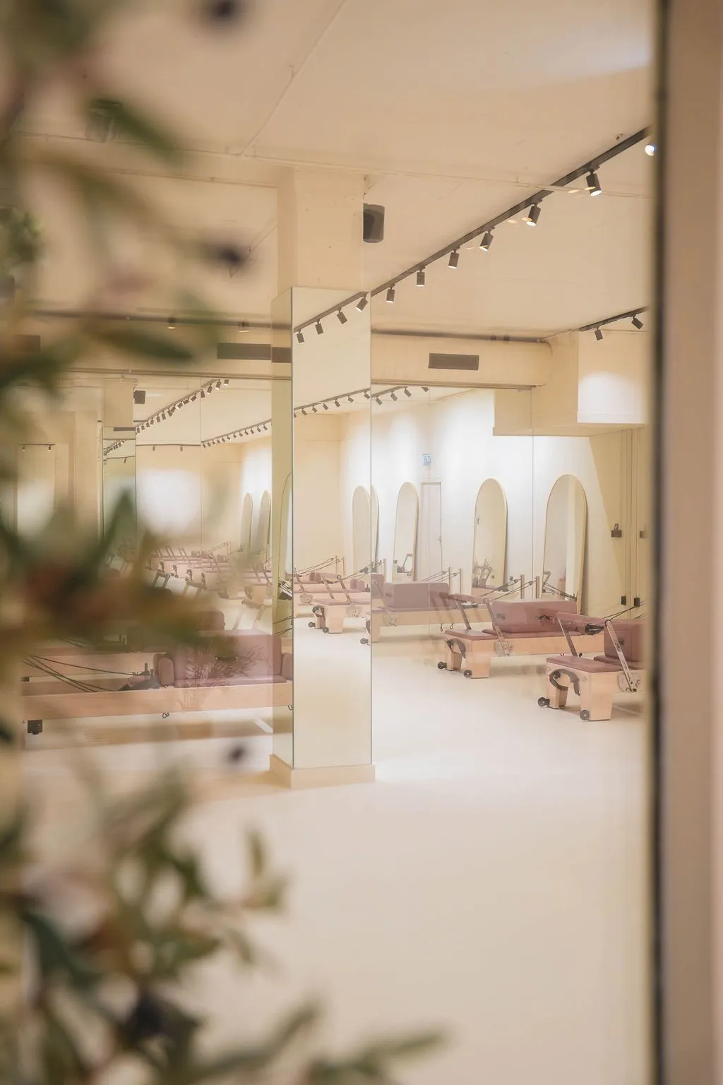 Lichte Pilatesstudio met houten reformerapparaten, grote spiegels en zachtbeige muren.
