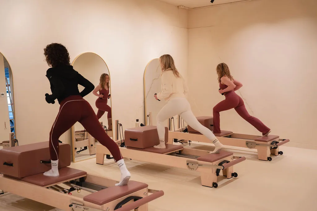 Persoon die een box op een Pilates reformer-apparaat verstelt in een lichtgekleurde ruimte.