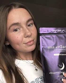 Young woman with long brown hair holding a purple pouch of RoaDrams, a dietary supplement drink mix.