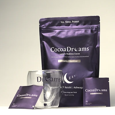 Purple packaging of CocoaDreams luxury bedtime cocoa with a transparent glass and two cocoa sachets.