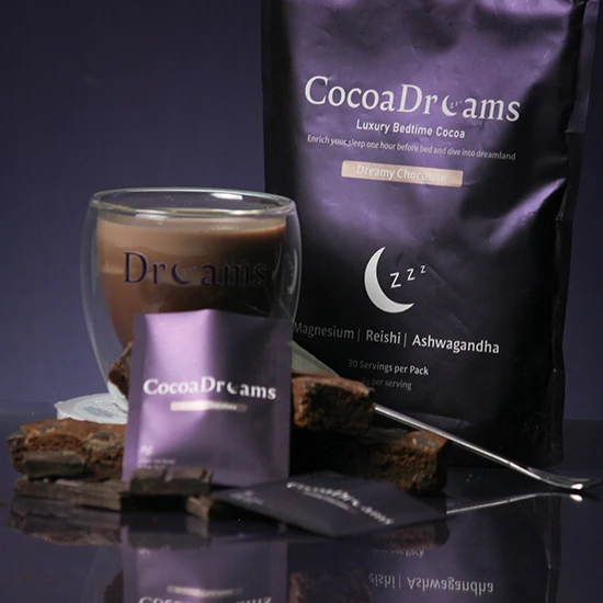 Cocoa Dreams Luxury Bedtime Cocoa package, a glass of prepared cocoa, and cocoa snack packets on a reflective surface with brownies.