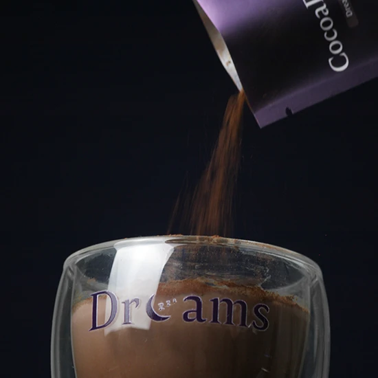 Chocolate powder being poured from a container into a glass cup labeled 'Dreams'.