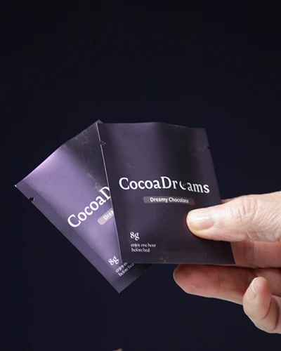 Hand holding two small black CocoaDreams Dreamy Chocolate packets.