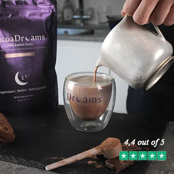 Hand holding two black packets of CocoaDreams Dreamy Chocolate powder against a dark background.