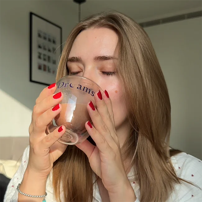 Chocolate powder being poured from a container into a glass cup labeled 'Dreams'.