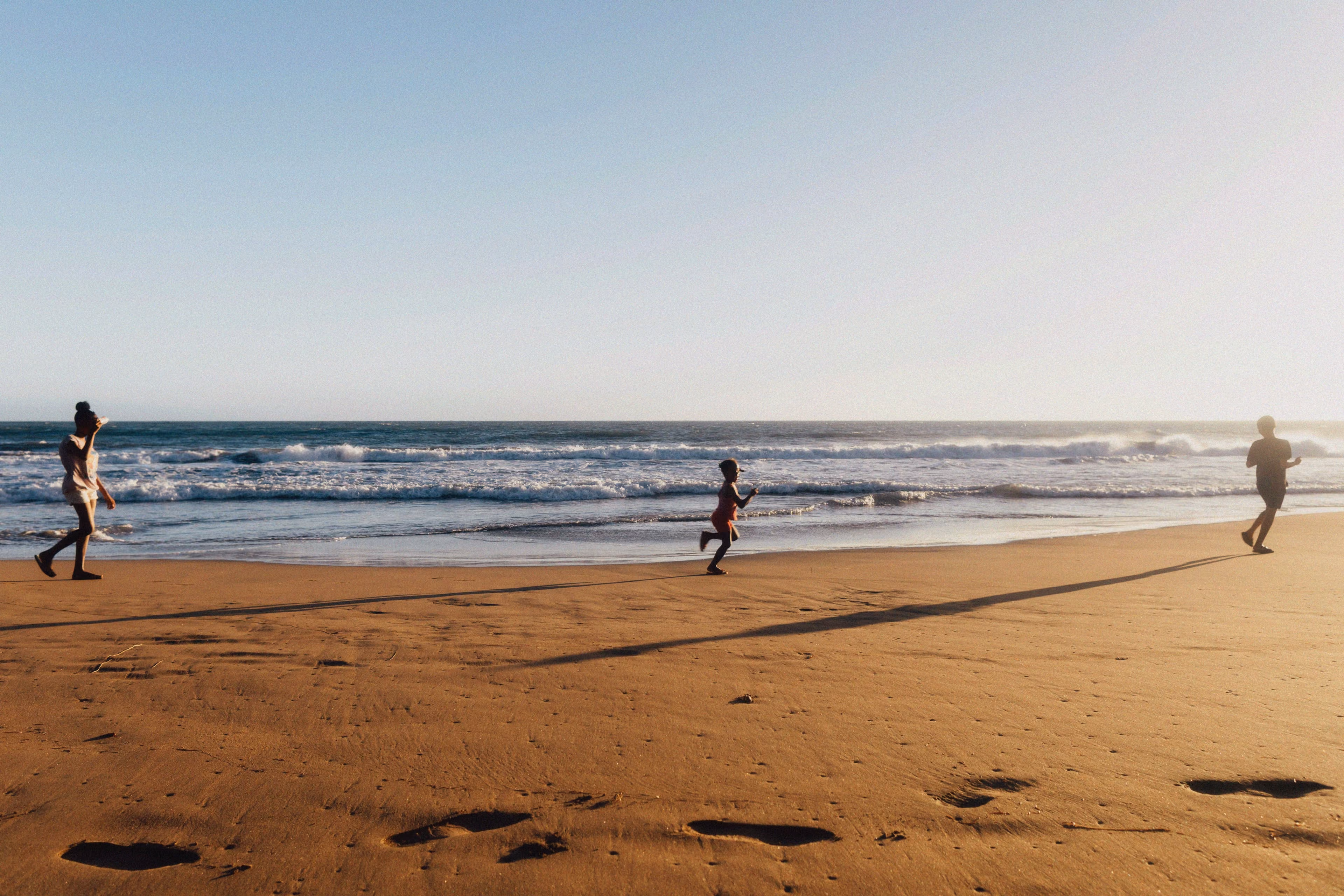 People walking and running along a sandy beach beside the ocean.