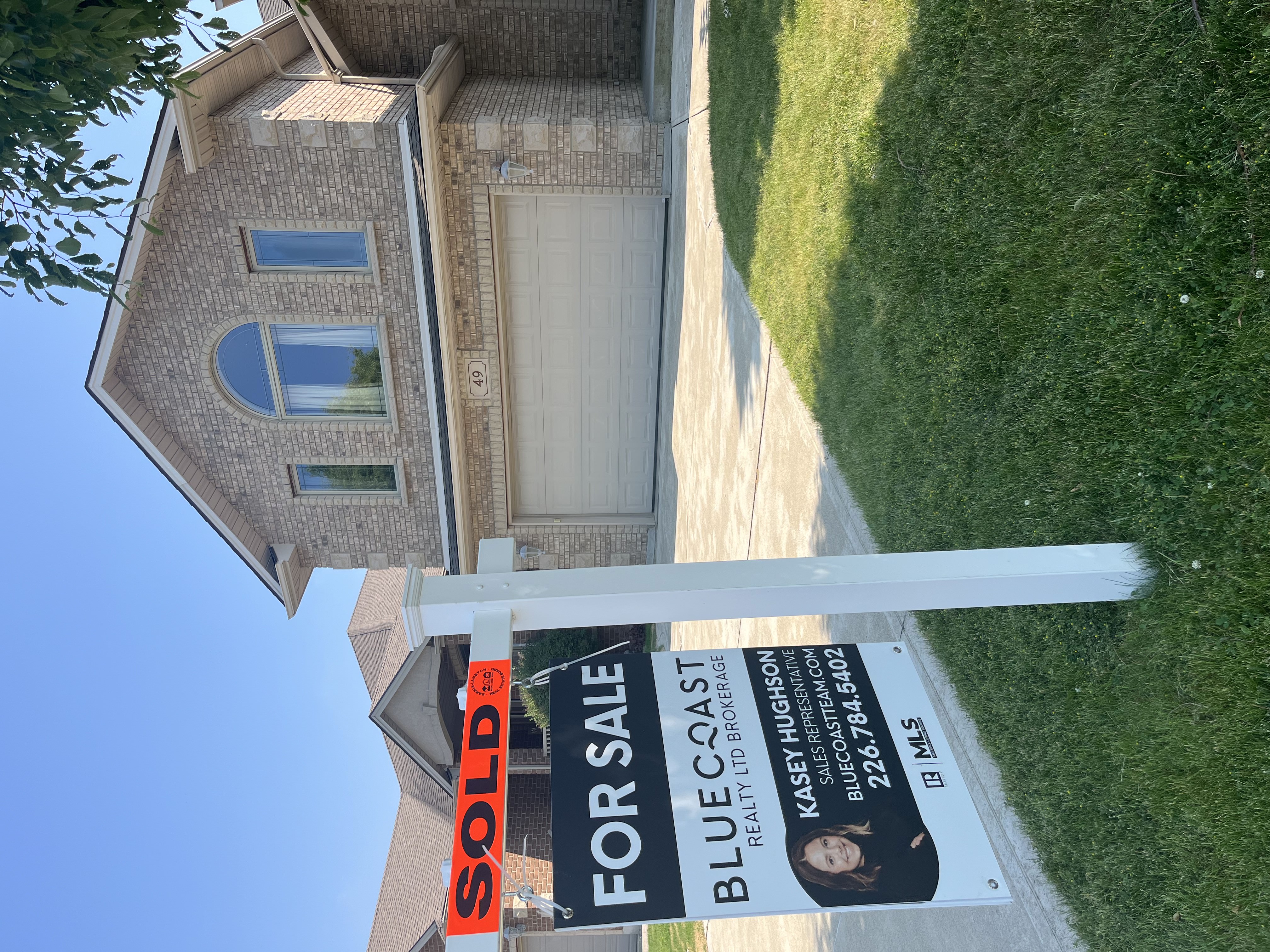 Young couple standing outside a brick townhouse with a small dog, next to a sold real estate sign.
