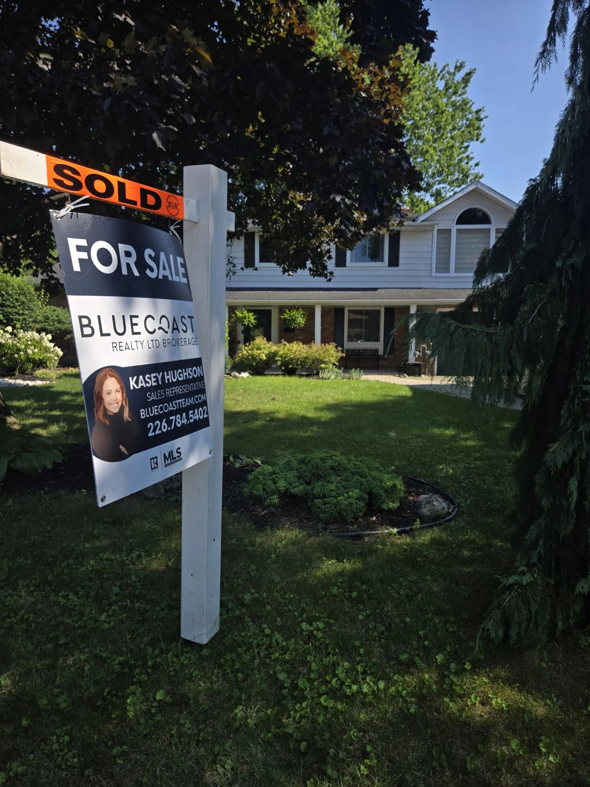 Sold sign in front of a two-story house with a green lawn and landscaping.
