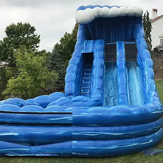 Large blue inflatable water slide with three sliding lanes and a ladder, set outdoors near trees and a building.