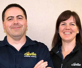 Smiling man and woman wearing black Castle building centres shirts against a plain wall.
