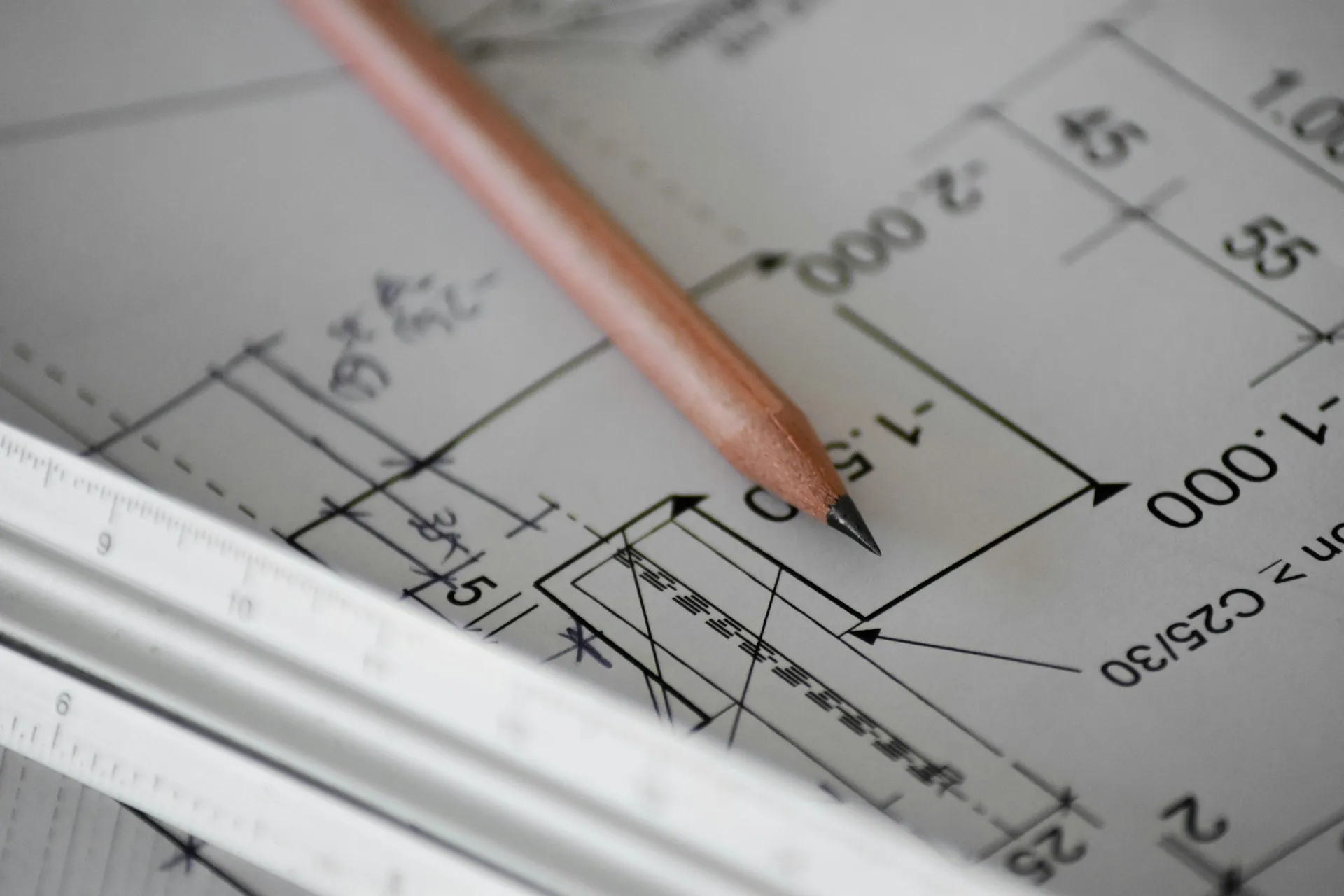Close-up of a sharpened pencil and a ruler on an architectural blueprint with measurements and technical drawings.
