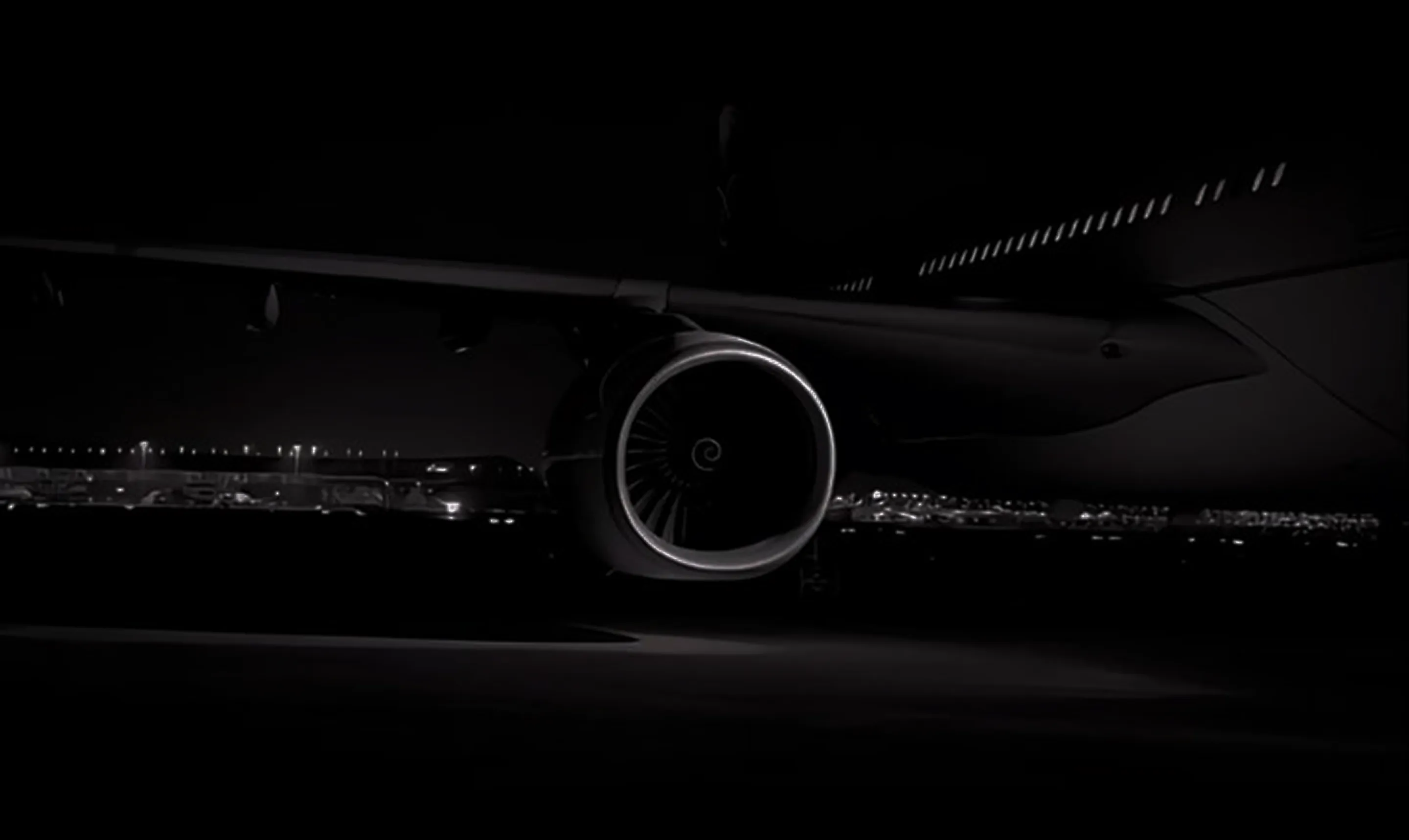 Close-up of a plane engine on the wing at night with airport lights in the background.