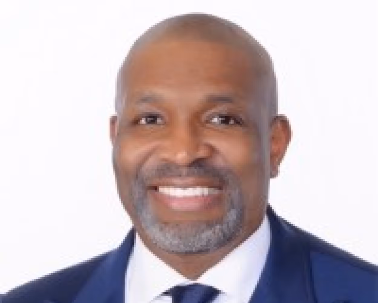 Smiling LaMont Cole with a beard wearing a dark blue suit, white shirt, and tie against a white background.