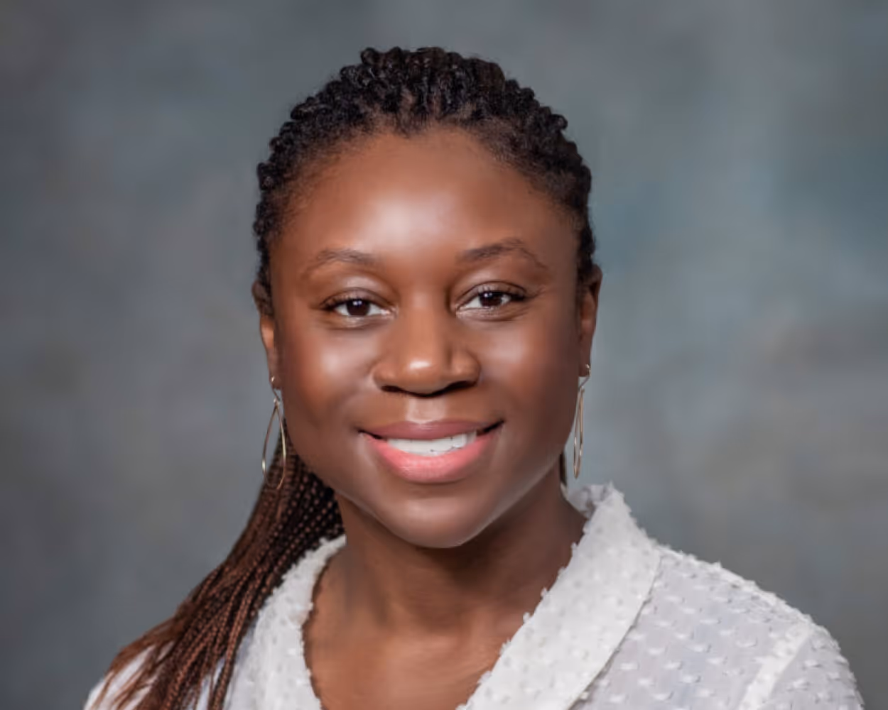 Smiling Janelle with braided hair wearing a white textured blouse against a gray background.