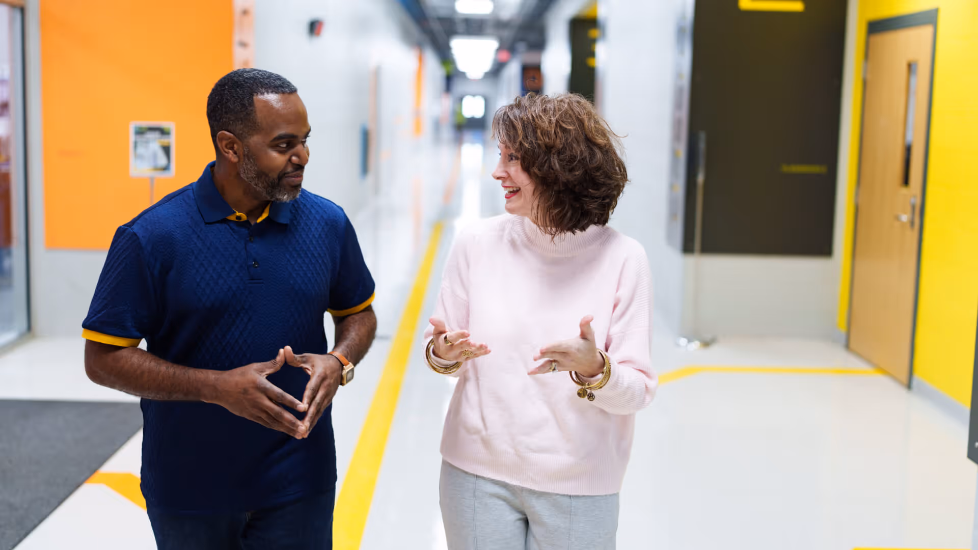 Two people walking and talking through a modern industrial hallway with large "A" and "2" signage.