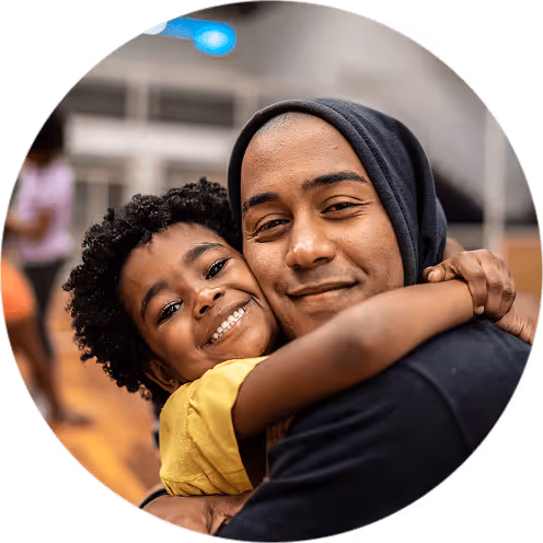Smiling child in a yellow shirt hugging a man wearing a black hoodie, both looking at the camera.